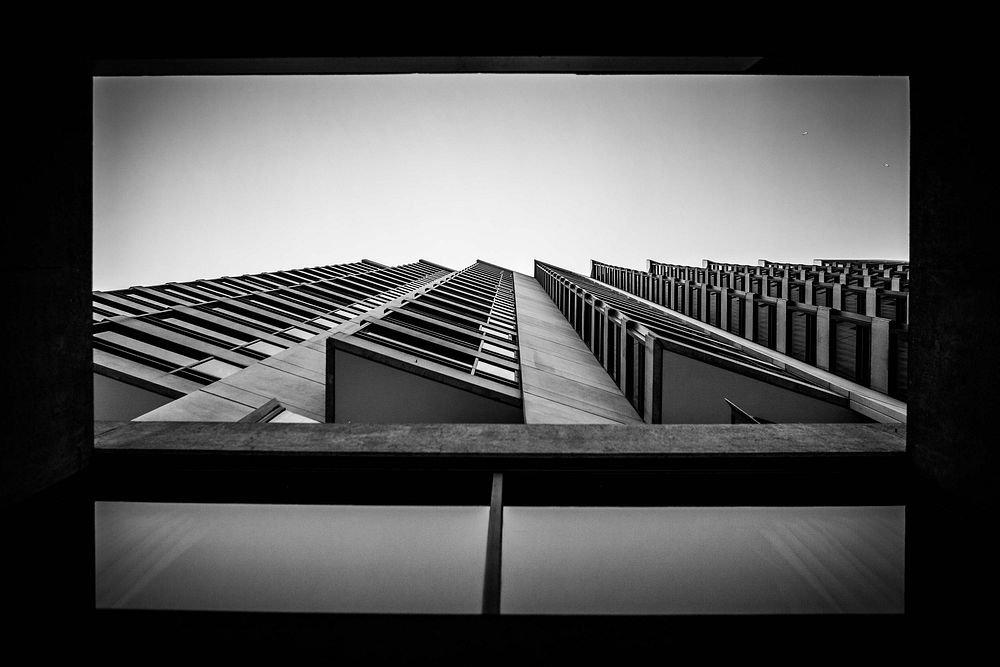 A low-angle shot of a banister and overhanging windows in the facade of a high-rise. Original public domain image from…
