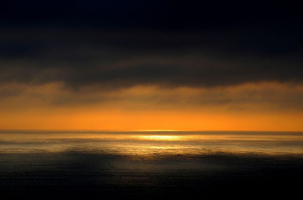 A dark and moody sunset over the ocean with yellow and orange rays on the horizon in Chile.. Original public domain image…