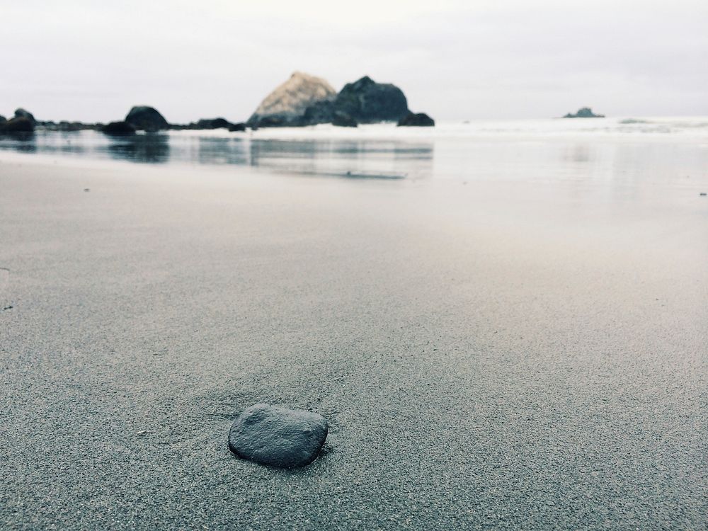 Small rock on the fine wet sand beach coast. Original public domain image from Wikimedia Commons