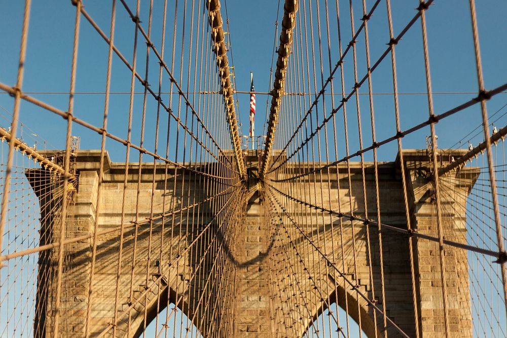 American flag on top of a tower in the Brooklyn Bridge seen through bridge wires. Original public domain image from…