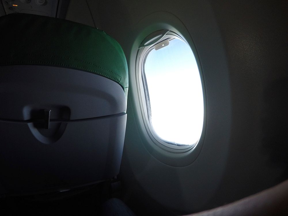 A round airplane window with pale light shining through it. Original public domain image from Wikimedia Commons
