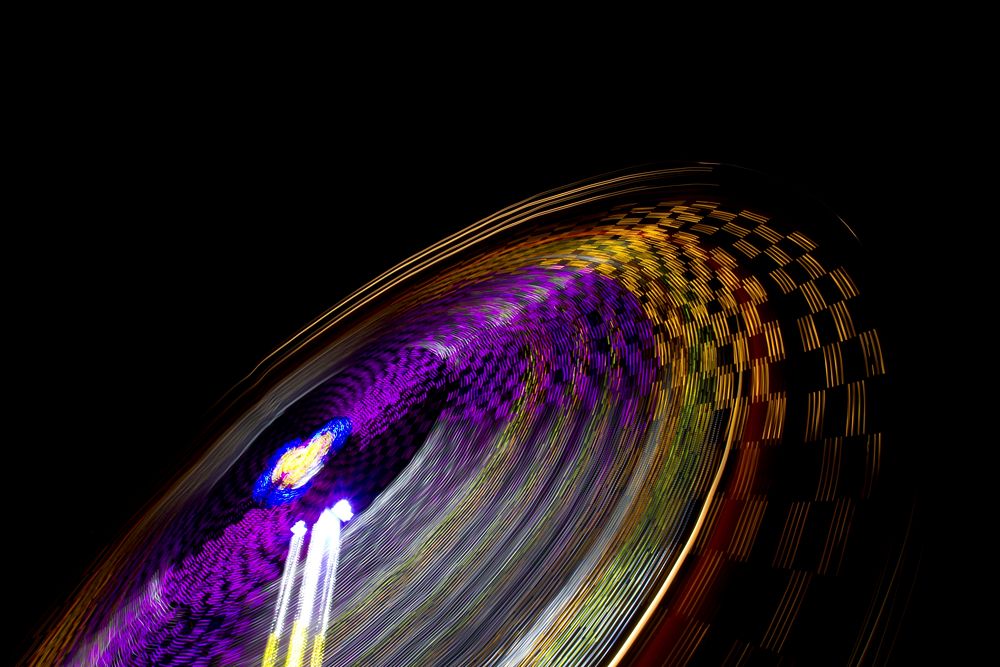 A blurred shot showcasing colorful light trails from a spinning amusement park ride. Original public domain image from…