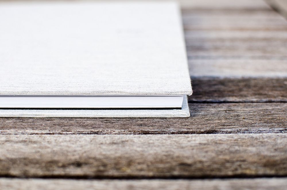 White hardcover book sitting on the wooden table. Original public domain image from Wikimedia Commons