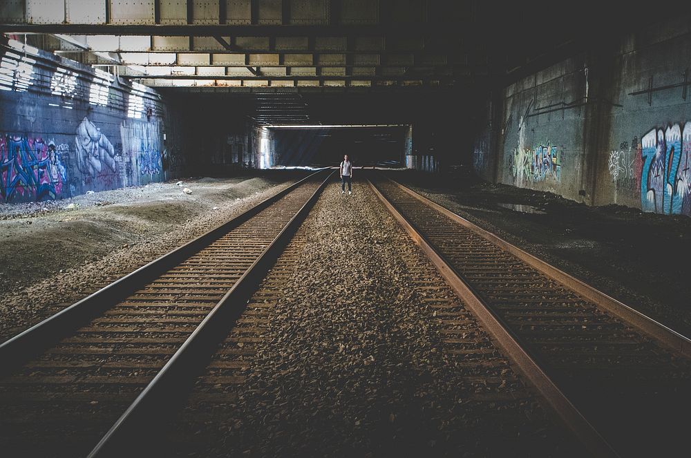 Person stands between underground train tracks in an urban environment. Original public domain image from Wikimedia Commons