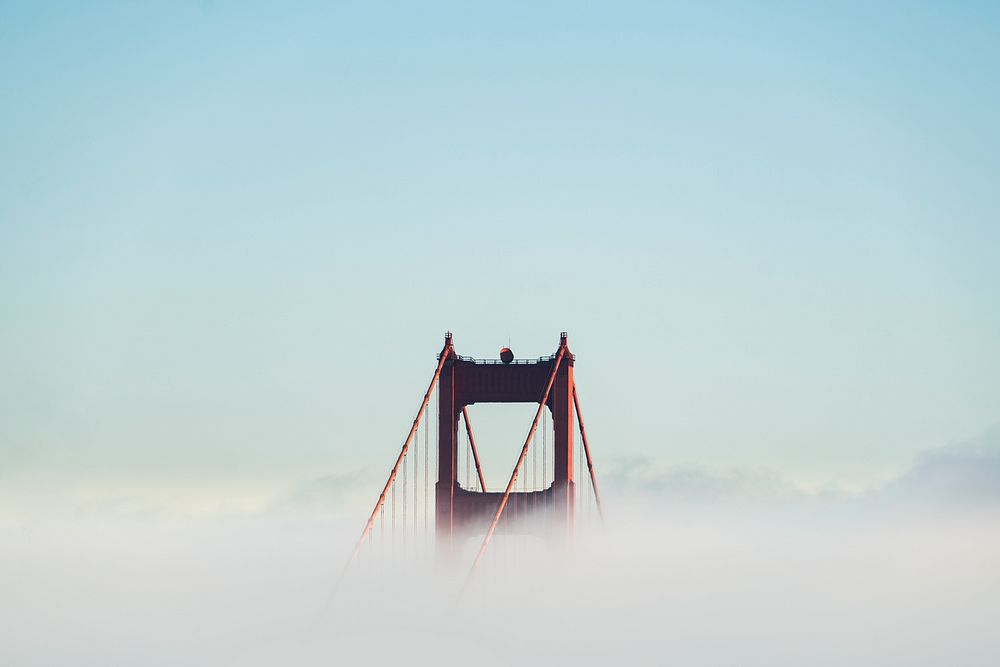 Golden Gate Bridge breaks through the clouds on a clear blue day. Original public domain image from Wikimedia Commons