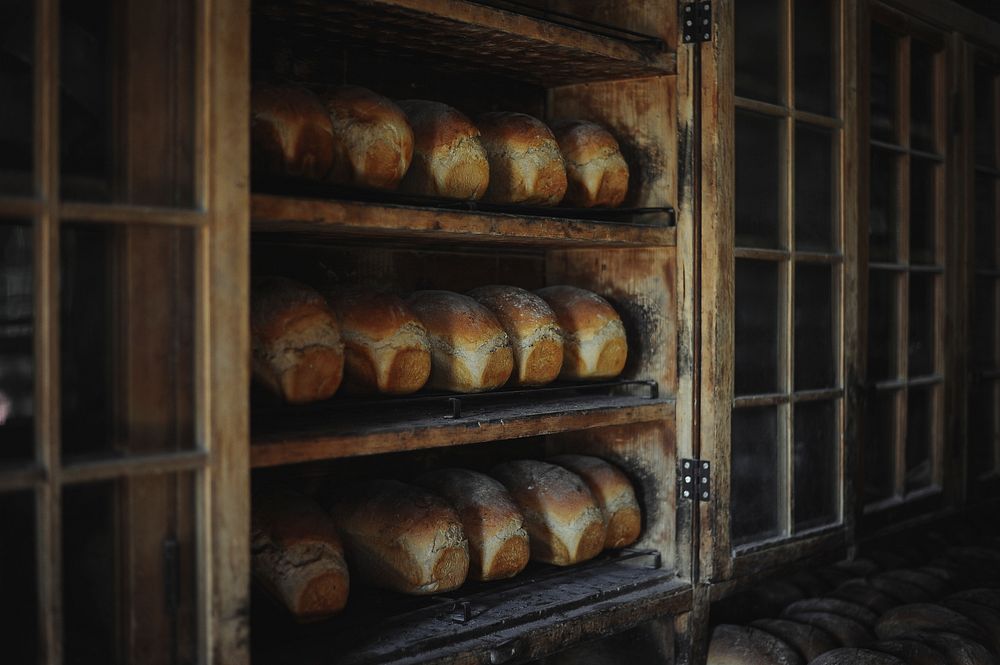 Loaves of baked bread in an old looking bakery on three wooden shelves with glass windows. Original public domain image from…