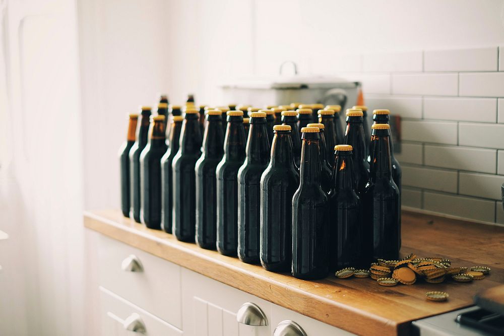 Beer bottle and their caps on a wooden drawer in the kitchen. Original public domain image from Wikimedia Commons