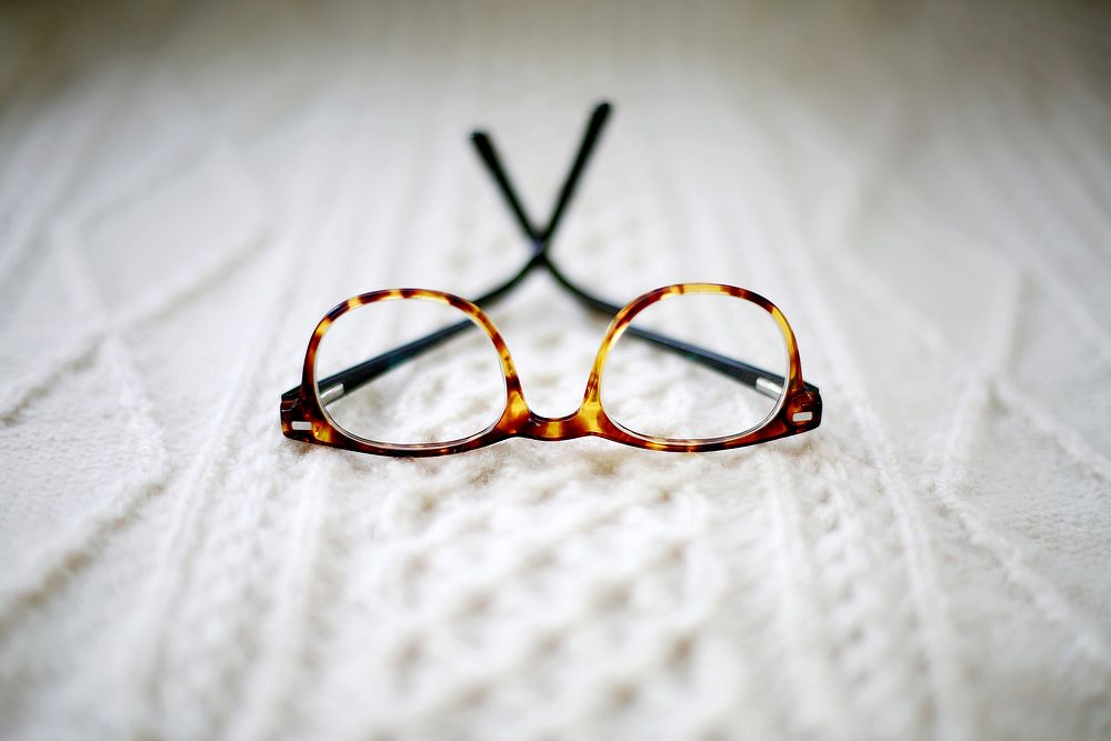 A pair of yellow speckled glasses resting upside down on a patterned white fabric. Original public domain image from…