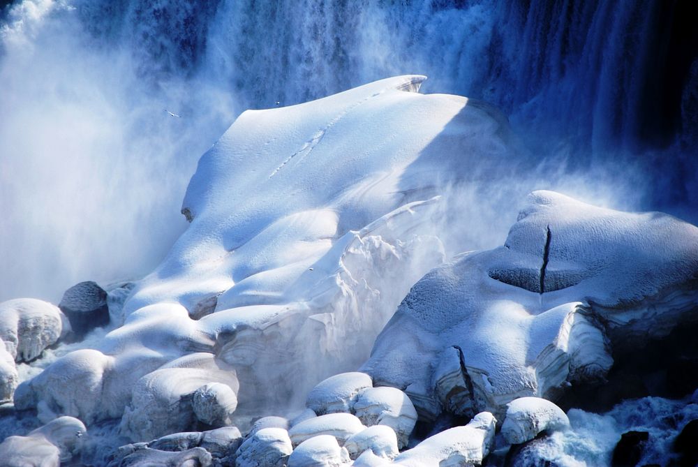 Snow covered a big rock in front of waterfall. Original public domain image from Wikimedia Commons