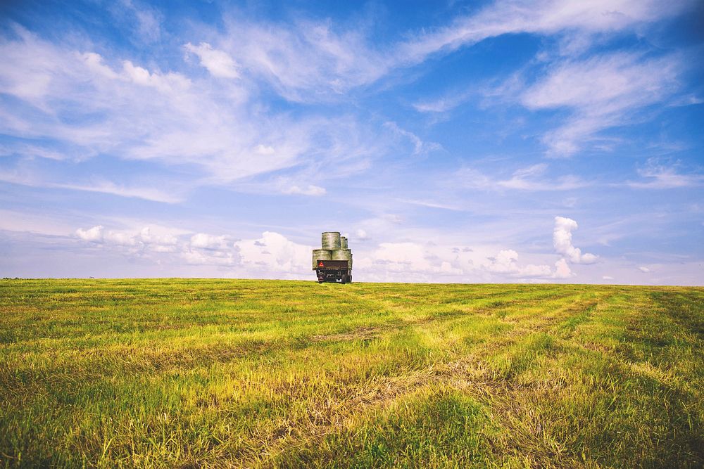 A green field and a truck driving off into the horizon where it meets the blue skies in Suchawa. Original public domain…