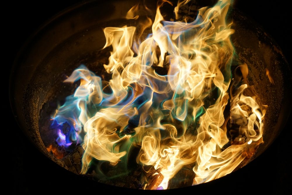 An orange fire with blue, purple, and green flames at night. Original public domain image from Wikimedia Commons