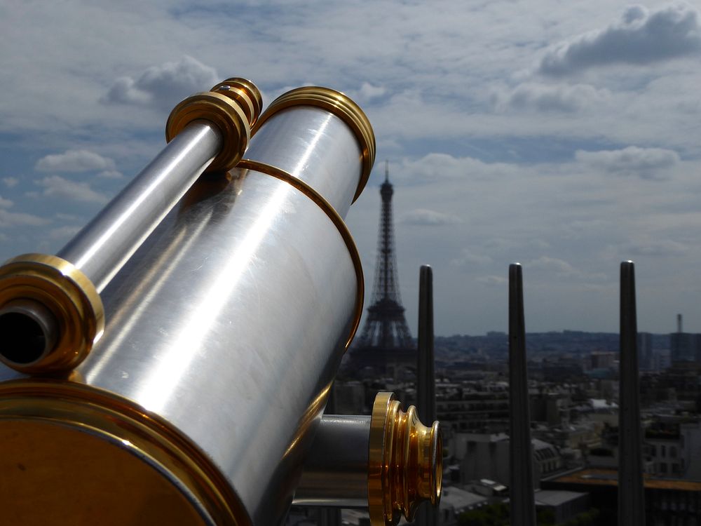 A metal viewfinder telescope with the historic Eiffel Tower and Paris cityscape in the background.. Original public domain…
