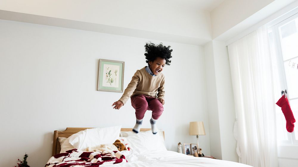 Young happy kid having fun jumping up and down on a bed