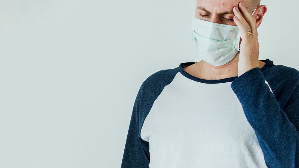 Sick man wearing surgical mask having a headache