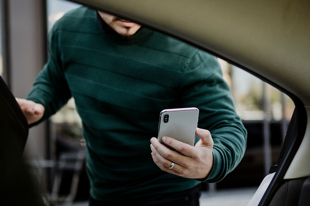 Man with his mobile phone entering a car