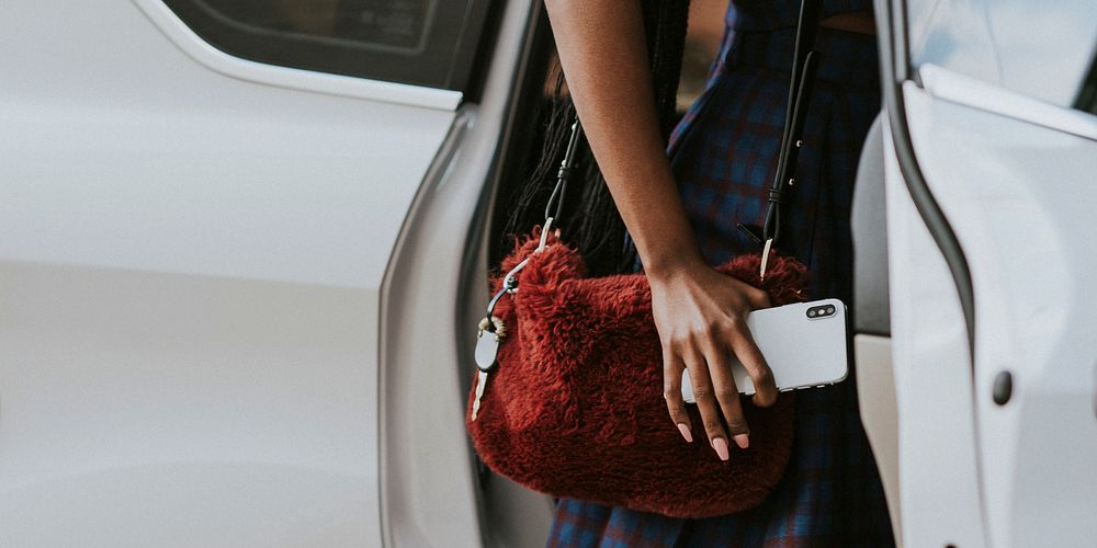 Black woman holding her phone while getting into a car