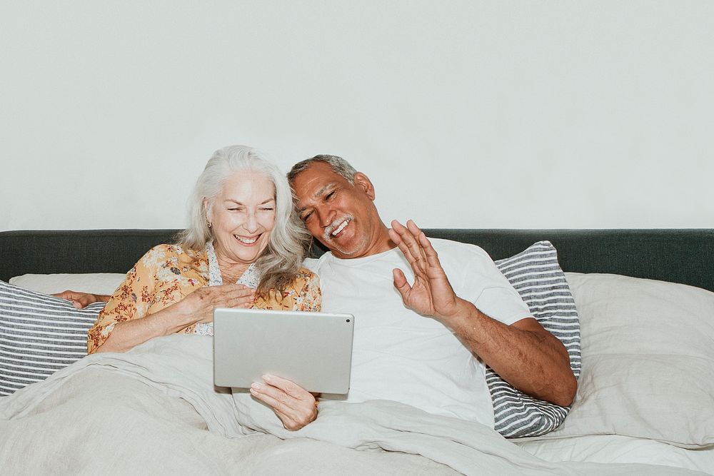 Elderly couple having a video call in bed