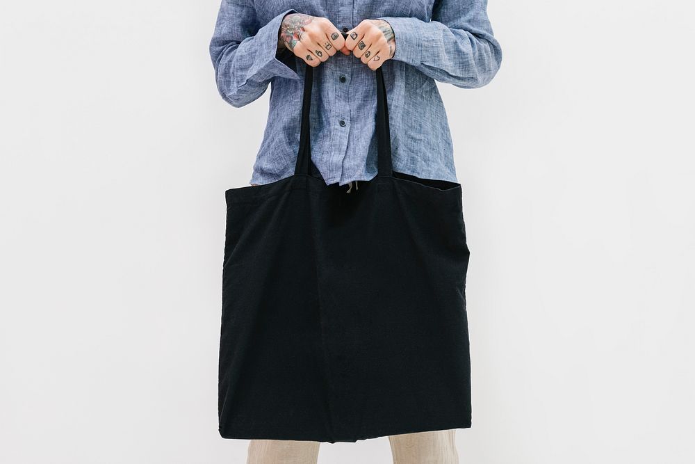 Tattooed woman in a blue linen shirt holding a black tote bag