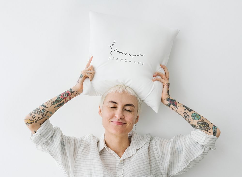 Tattooed woman holding a feminine pillow  over her head