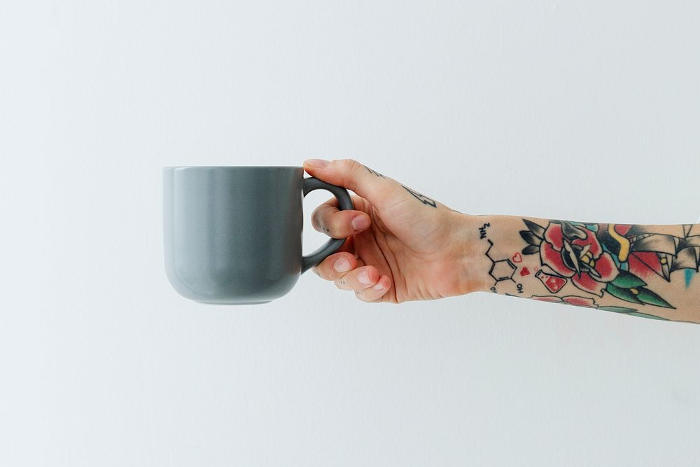 Tattooed hand holding a grayish blue coffee cup