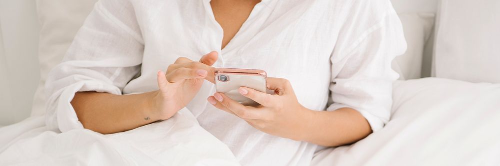 Woman using a phone on her white bed
