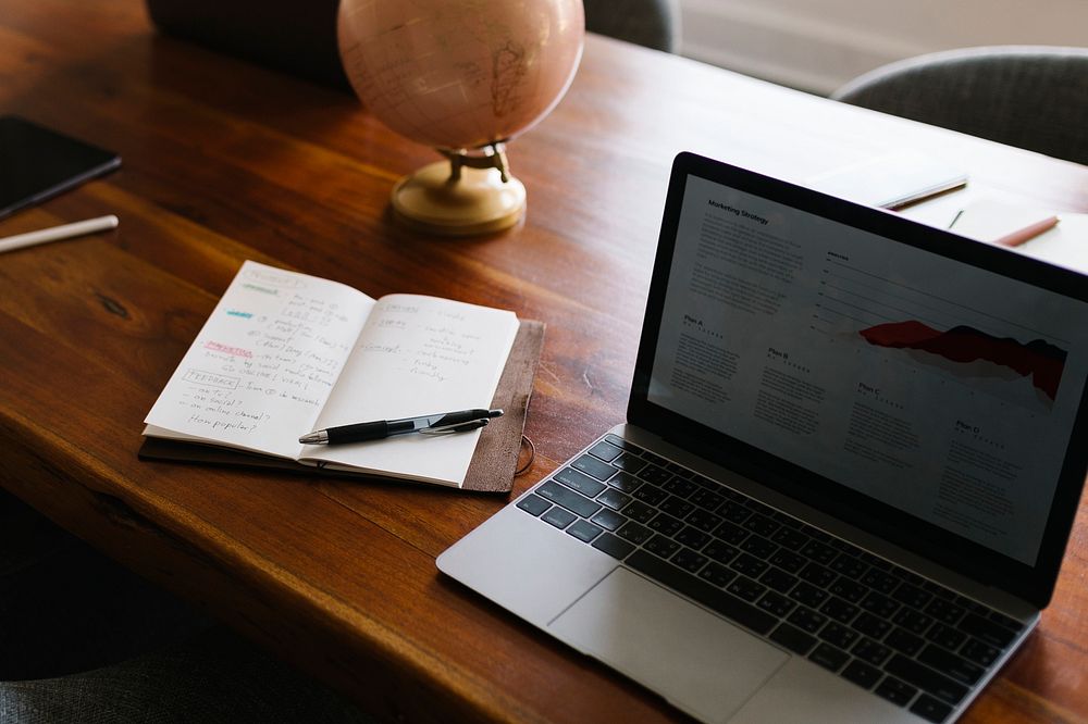 Laptop by a notepad on a wooden table in the office