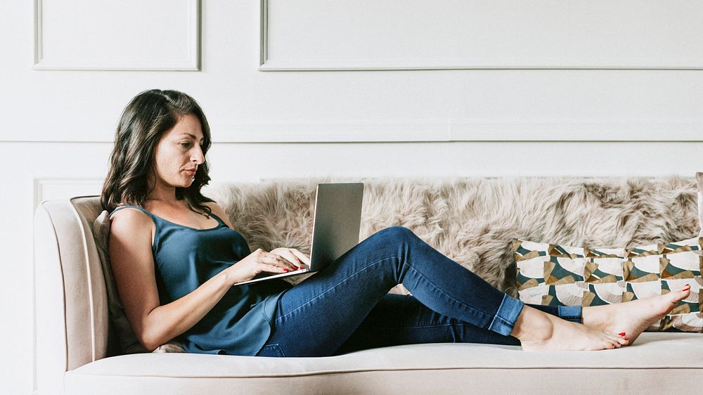 Casual woman working on her laptop while laying on the couch