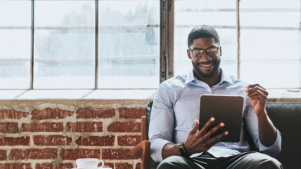 Cheerful black man using a stylus with a  digital tablet in a living room