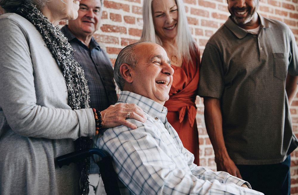 Happy elderly man on a wheelchair talking with friends