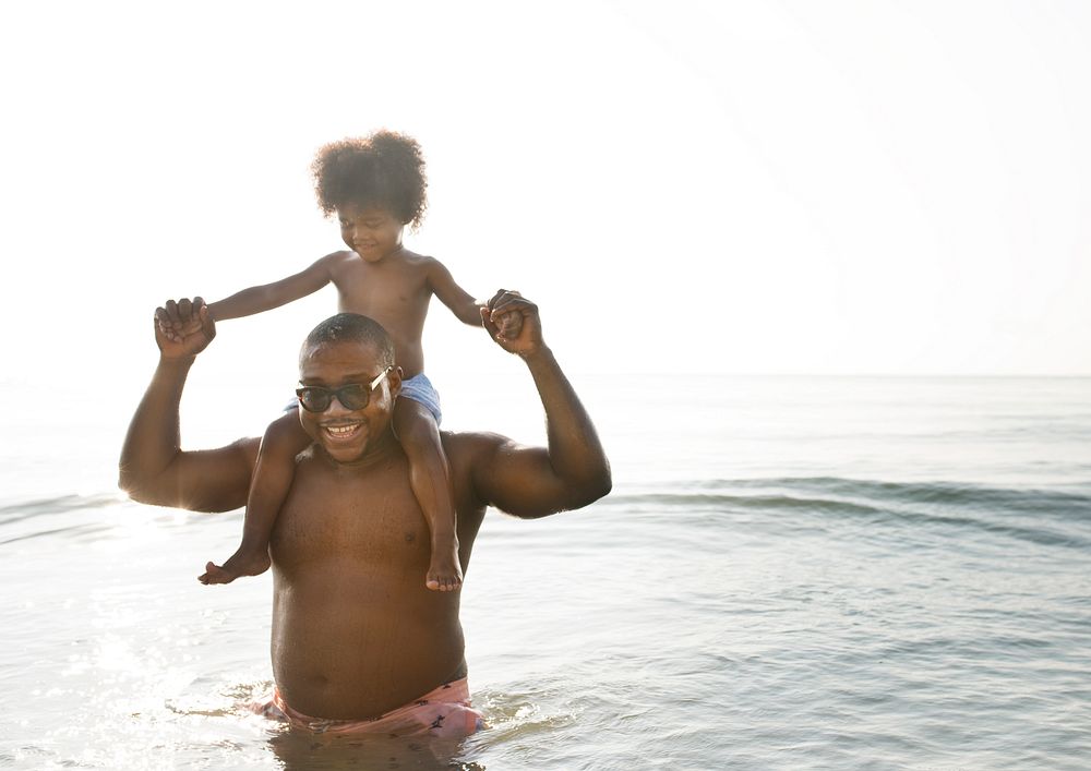 African American dad and son playing piggyback in the sea
