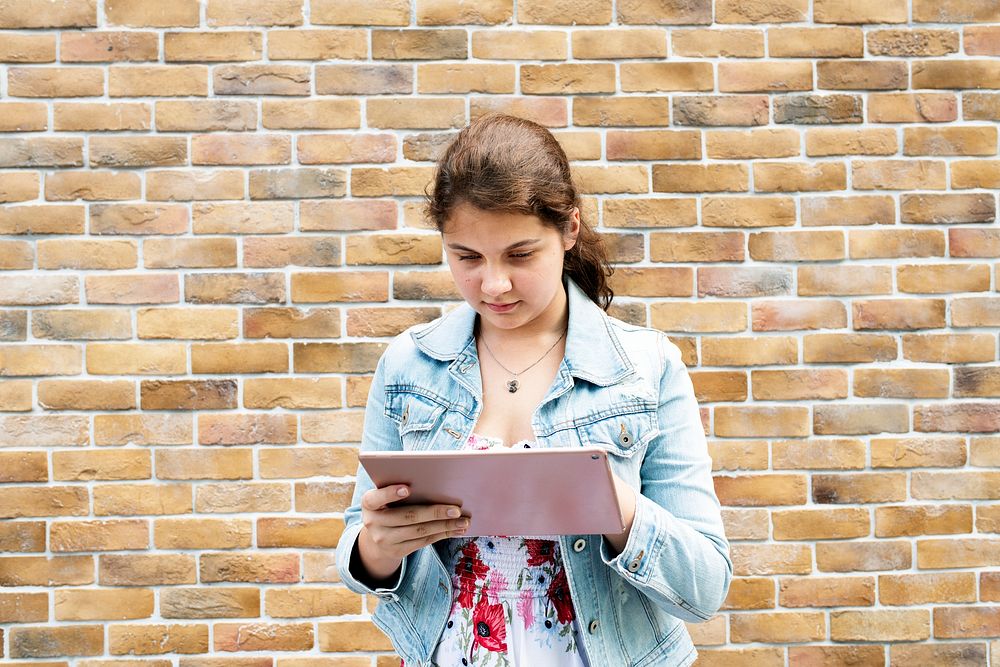 Girl using her tablet by a brick wall