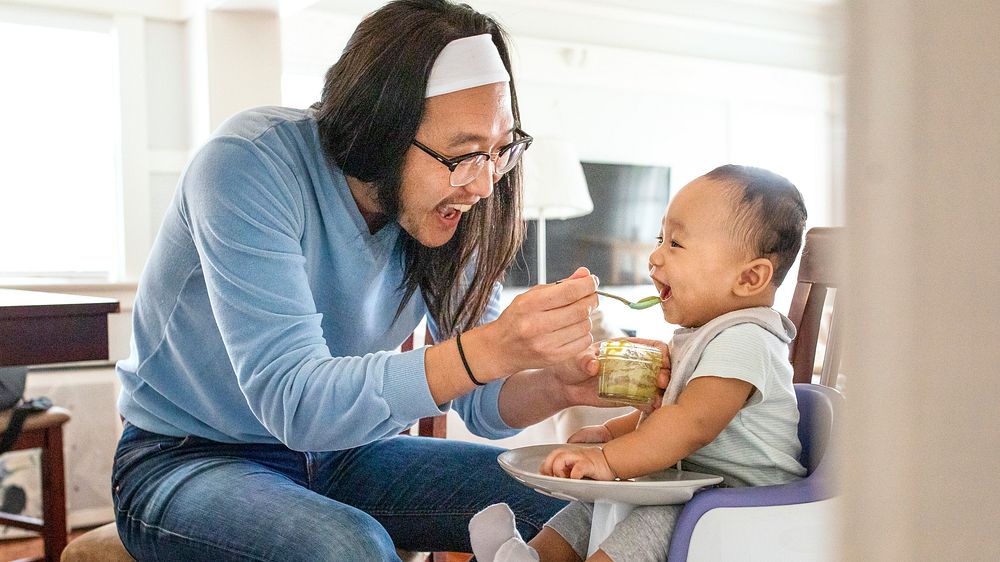 Asian father feeding his son on a highchair