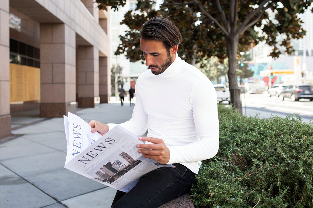 Businessman in turtleneck reading newspaper in the city