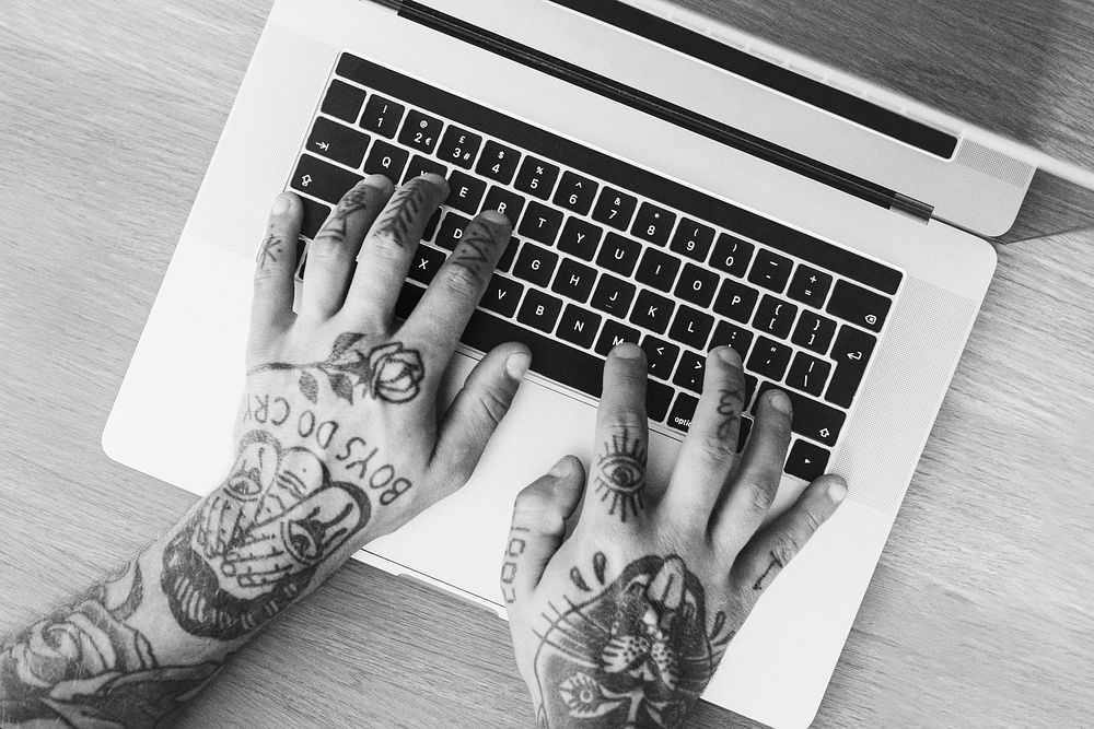 Man with tattooed hands typing on a laptop. 2 OCTOBER 2020 - CHIPPENHAM, UK