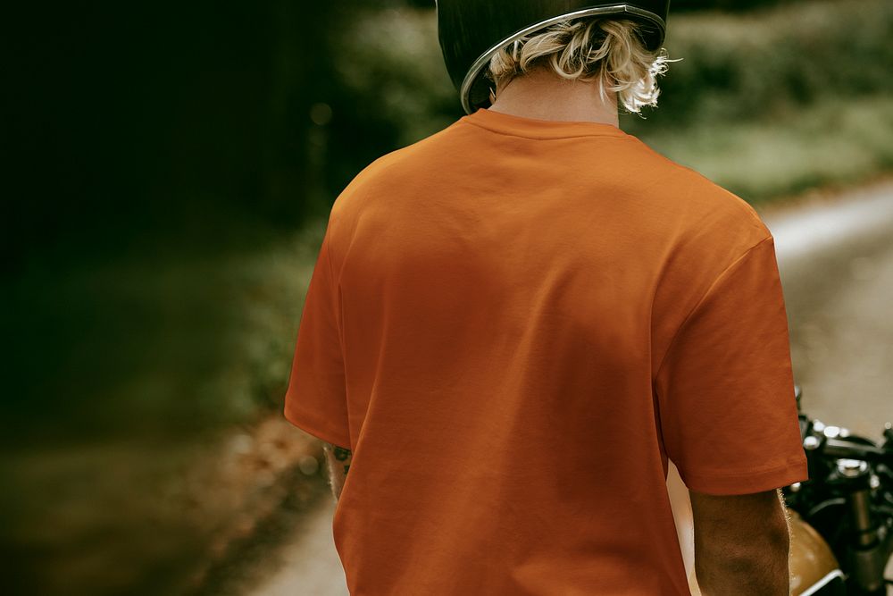 Blonde man in orange t-shirt sitting on a bike with design space