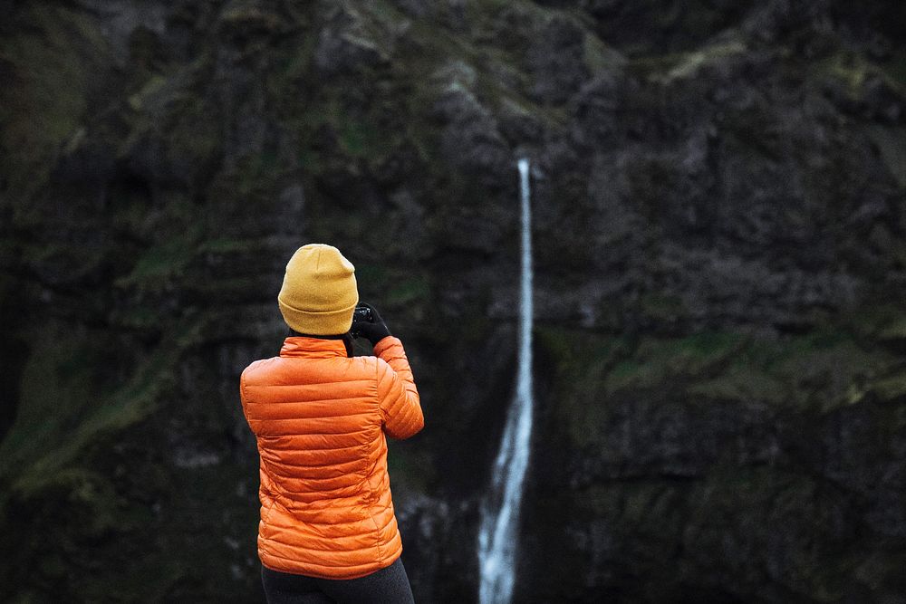 Rear view of a woman capturing a view of a waterfall