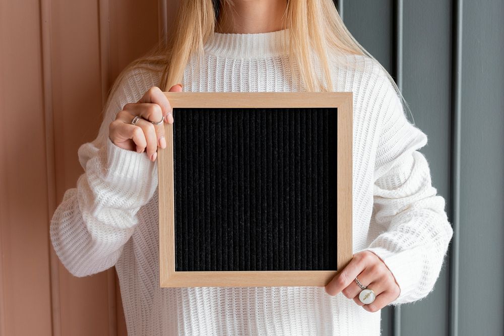 Woman in a white sweater holding a black wooden frame