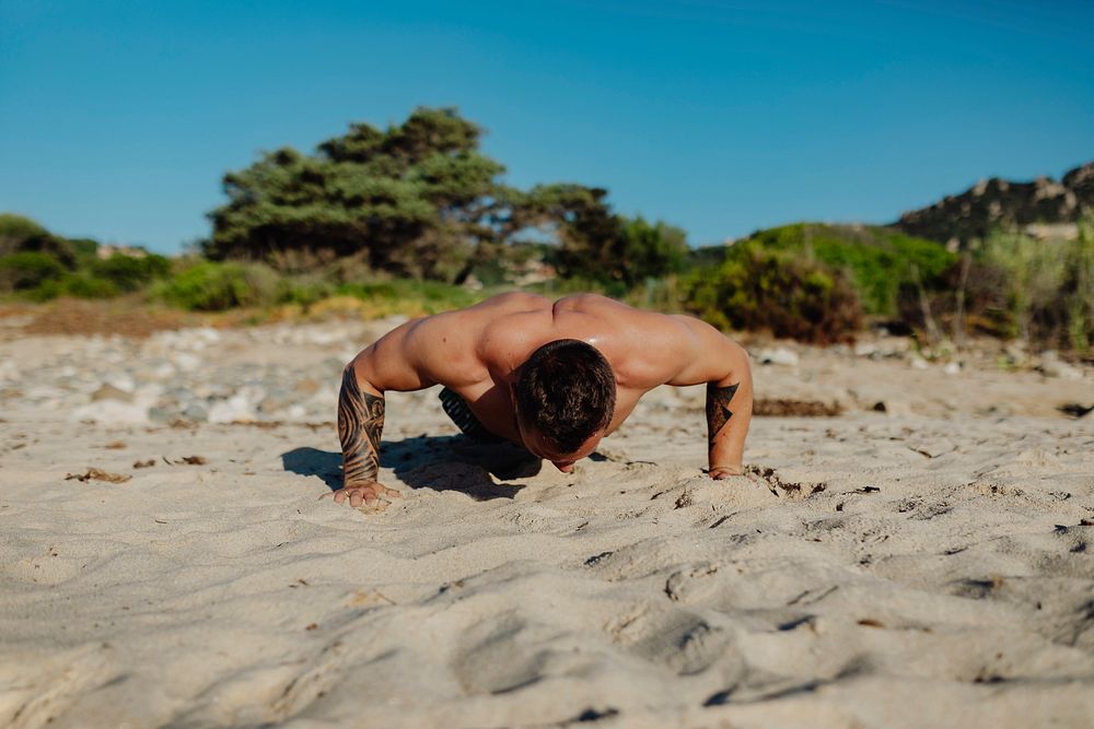 Tattoo man doing a push up at the beach