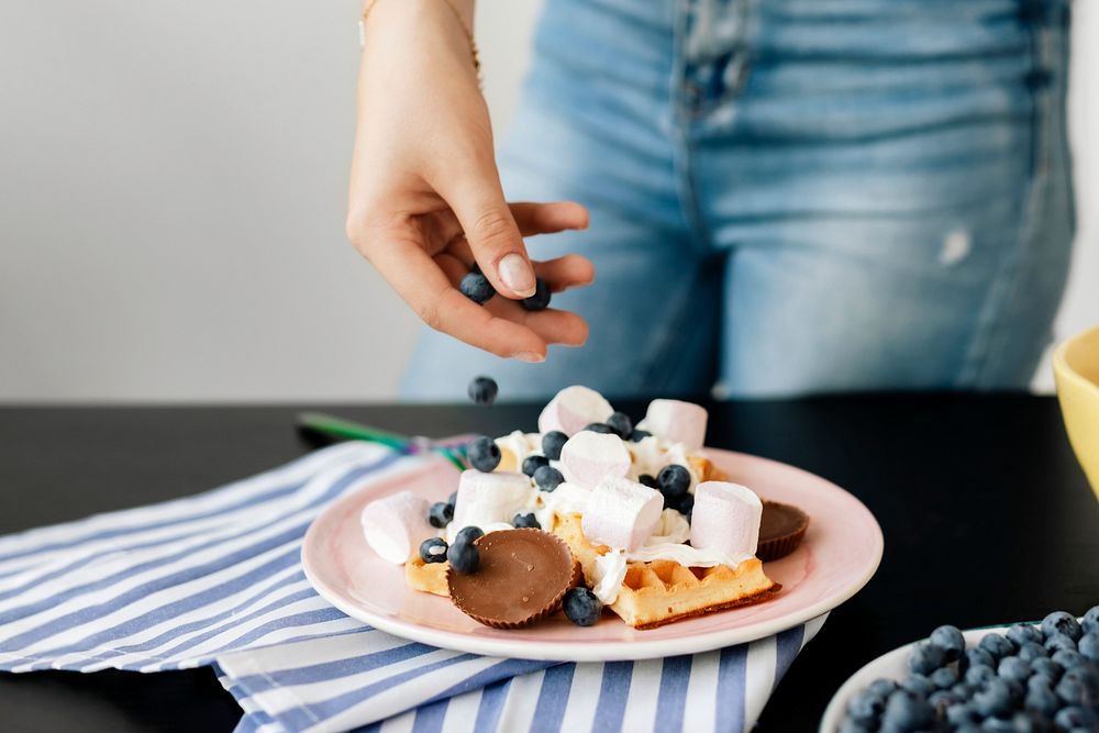 Woman topping her waffles with blueberries 