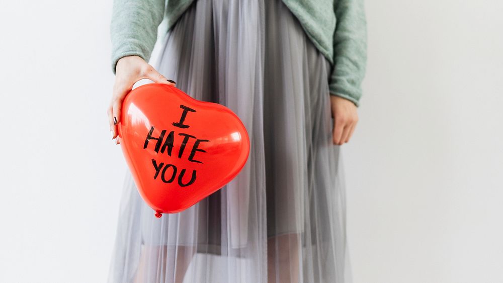 Woman showing a red heart balloon with I Hate You on it
