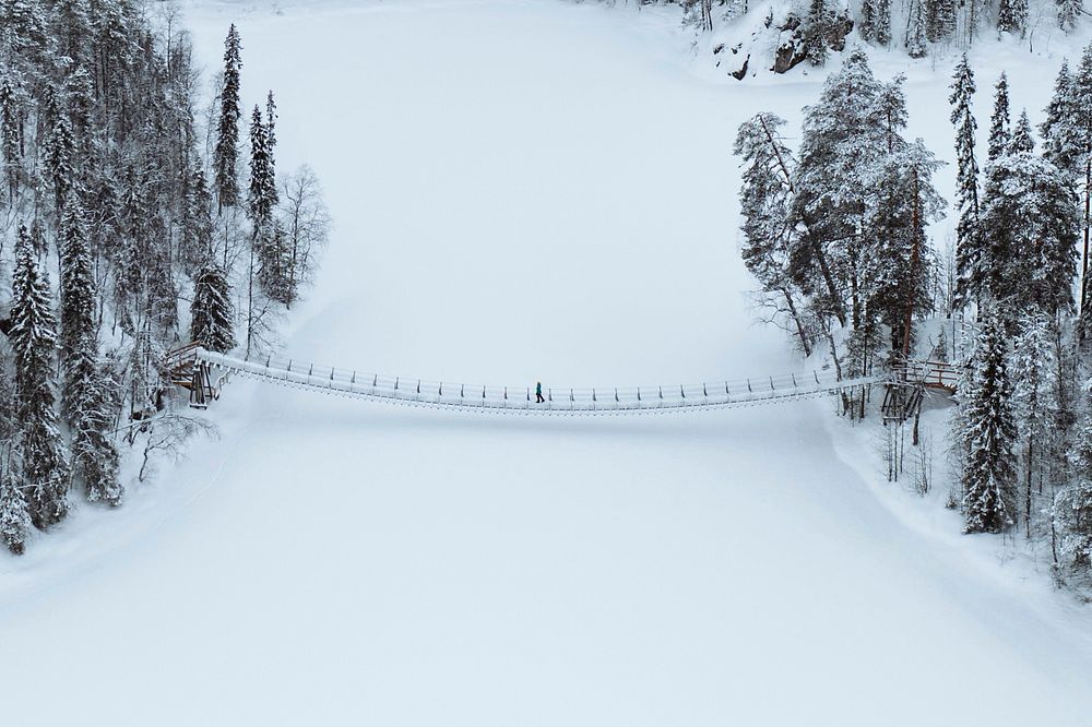 Woman crossing a suspension bridge in a snowy Oulanka National Park, Finland drone shot