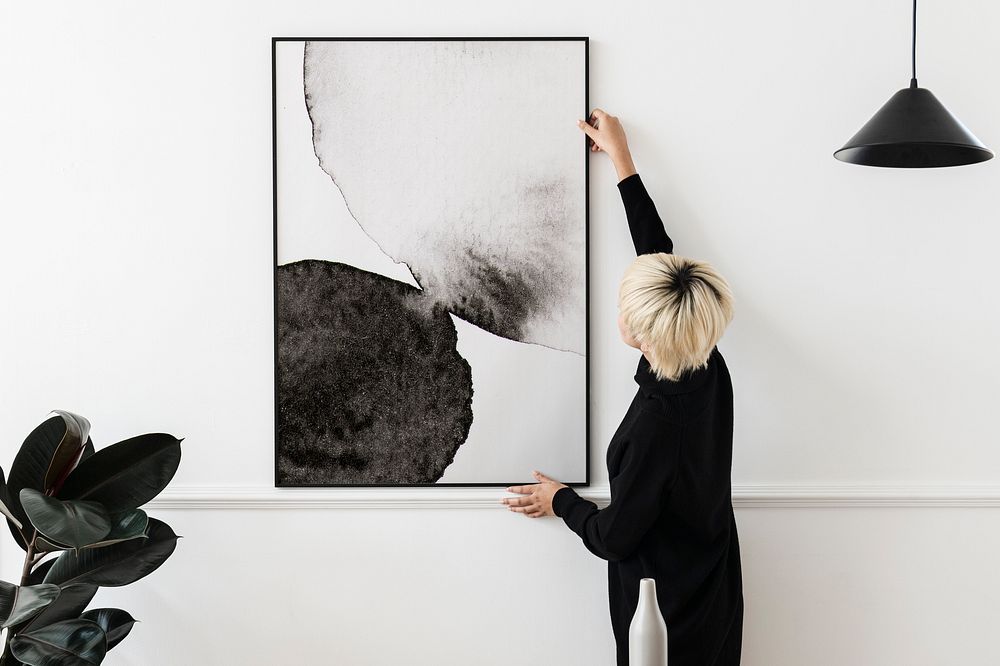Woman hanging black & white picture frame on white wall