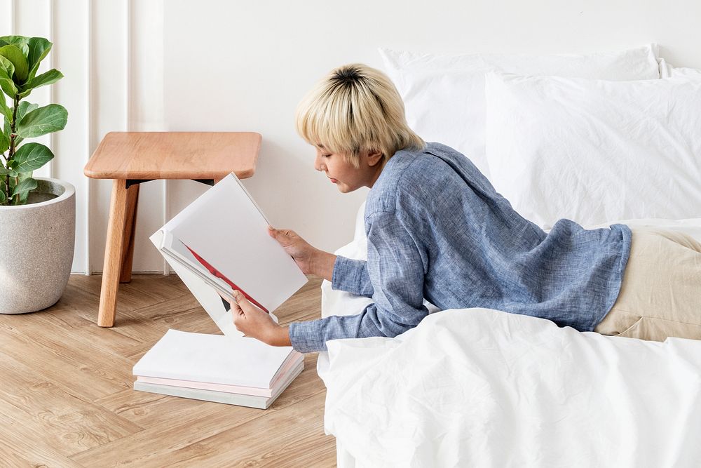 Blond haired Asian woman reading a book on a mattress on the floor