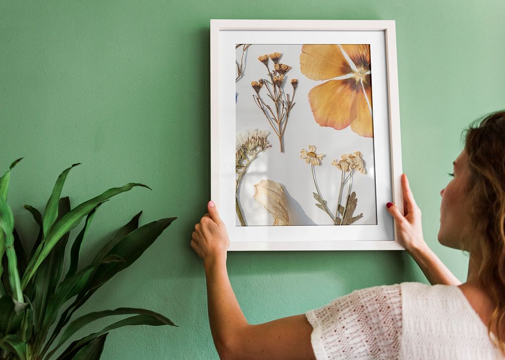 Woman hanging flower photo frame on a wall