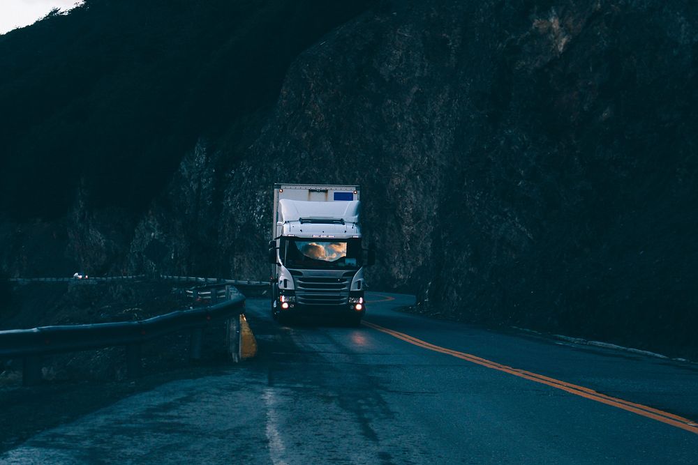 A silver Scania truck driving down an empty road in the mountains in the evening. Original public domain image from…