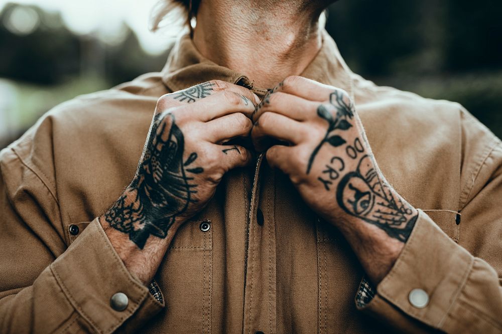 Tattooed man buttoning  brown shirt closeup