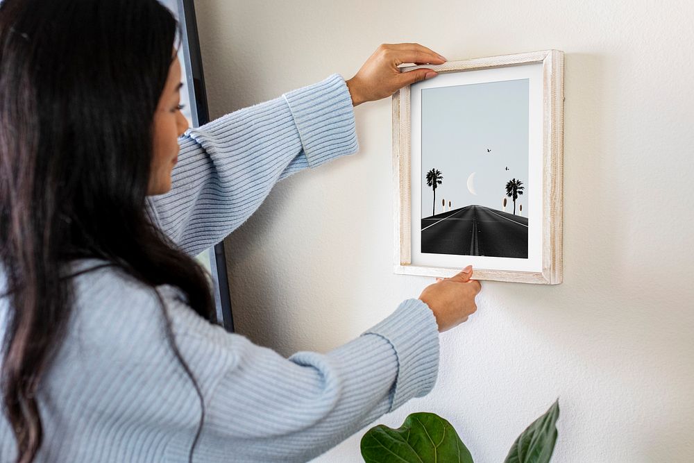 Woman hanging photo frame on white wall