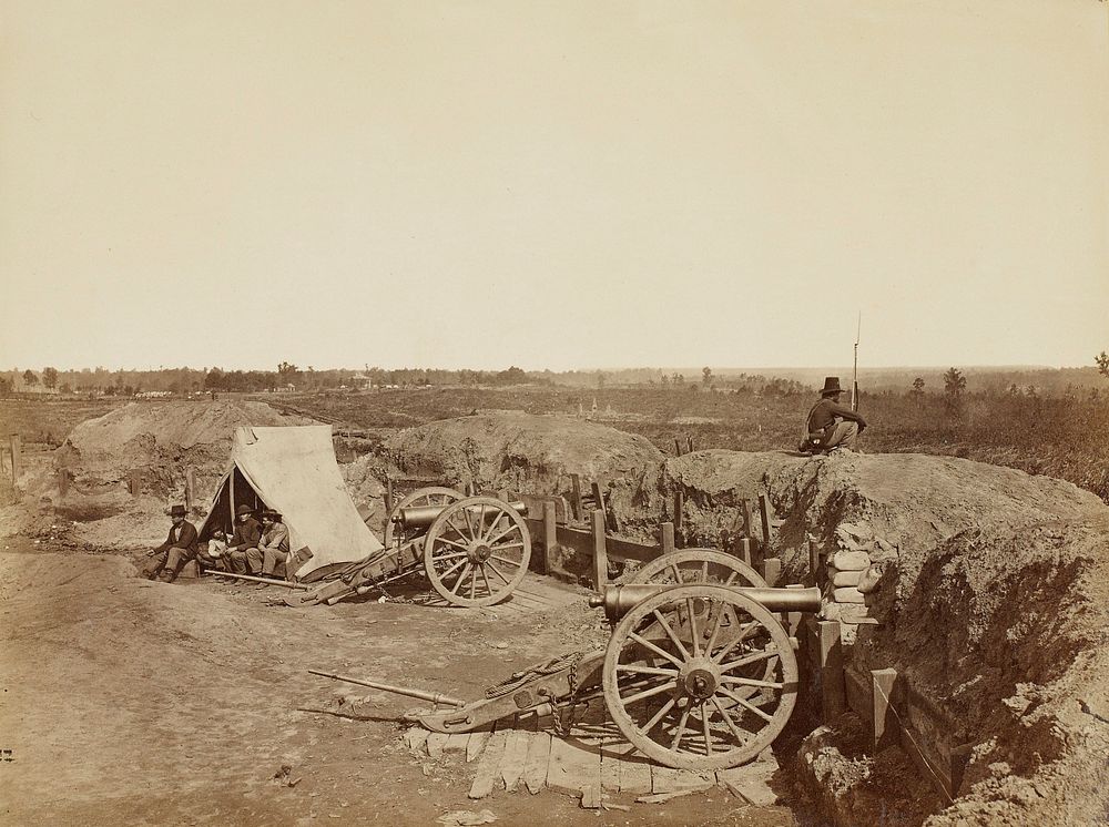 soldier with rifle seated on a dirt and sandbag barricade; two canons; four men sit in front of a tent at L. Original from…