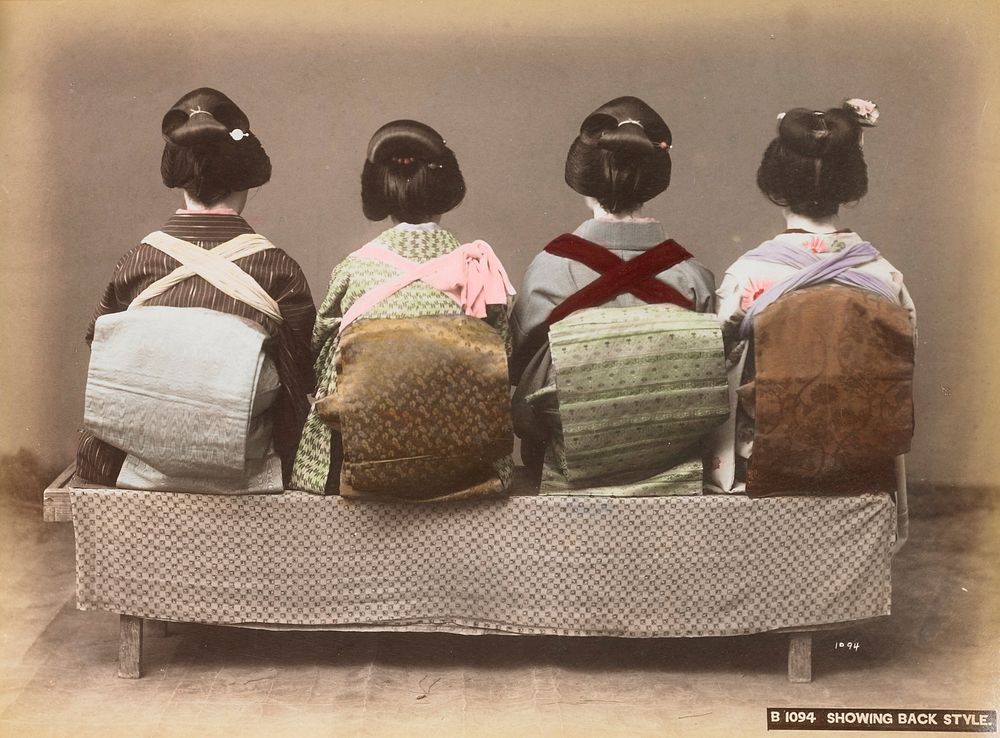 Four women seated on a bench covered with a patterned cloth, seen from back; women are wearing, from left: light blue obi…