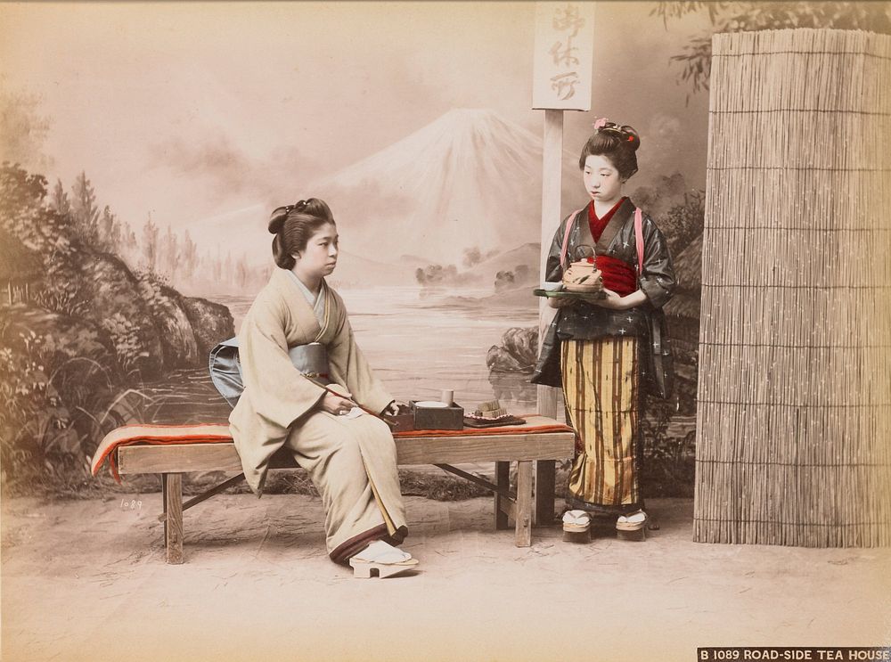 Woman seated on a bench, wearing a pale green kimono, blue obi and geta sandals, holding a small smoking pipe; young girl at…